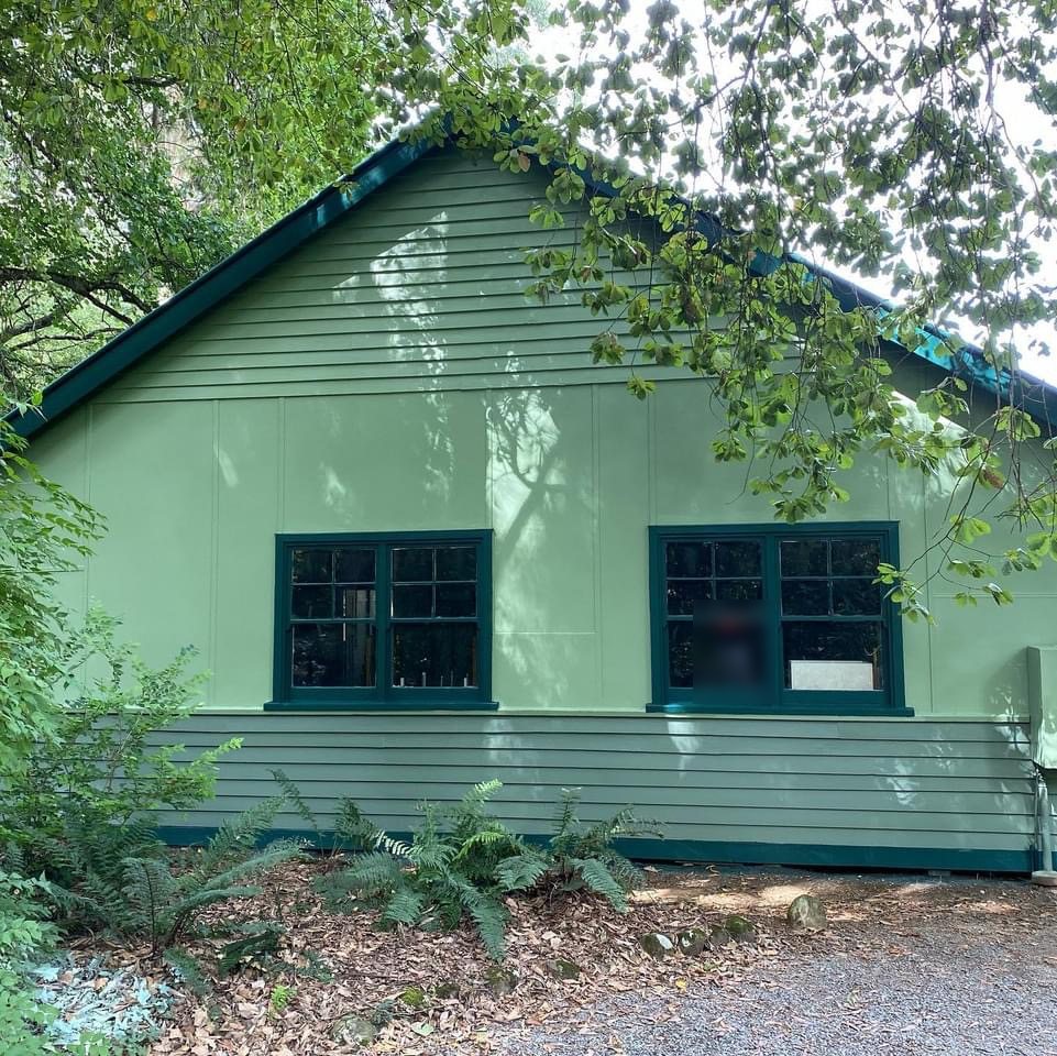 Weatherboard cottage painted sage green with dark green window frames and trim