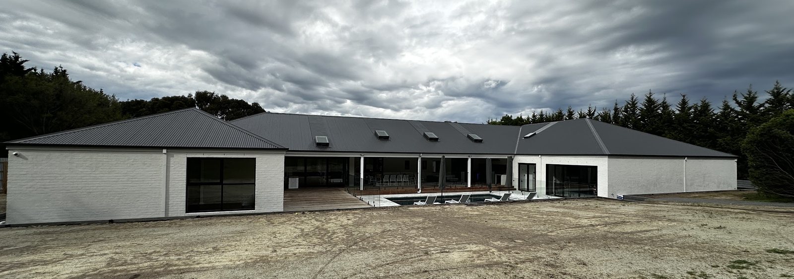 Long single-storey home with freshly painted white rendered walls under a stormy sky