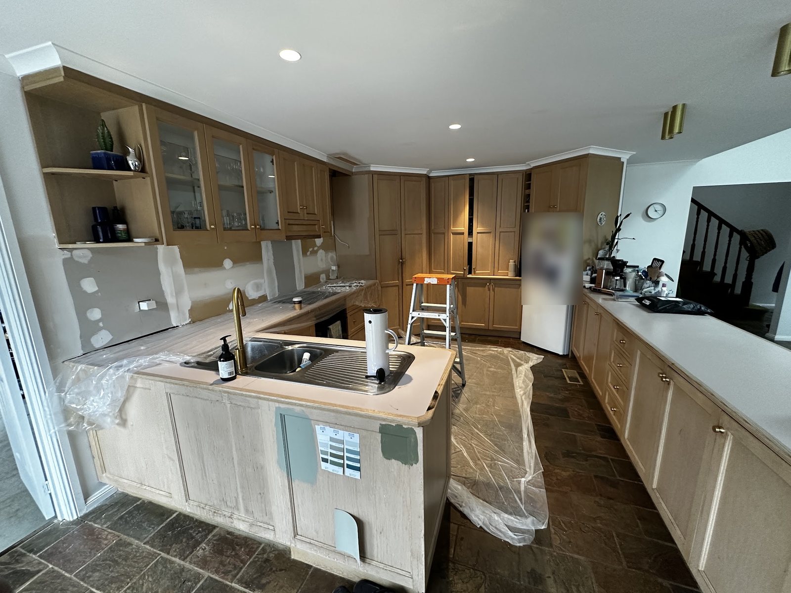 Kitchen mid-job with plastic sheeting over the floor, a ladder in place and paint colour samples on the cabinets